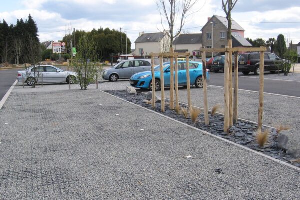 Mit dunklem Splitt verfüllter Parkplatz mit parkendenden Autos und Kleinstadt Gebäuden im Hintergrund