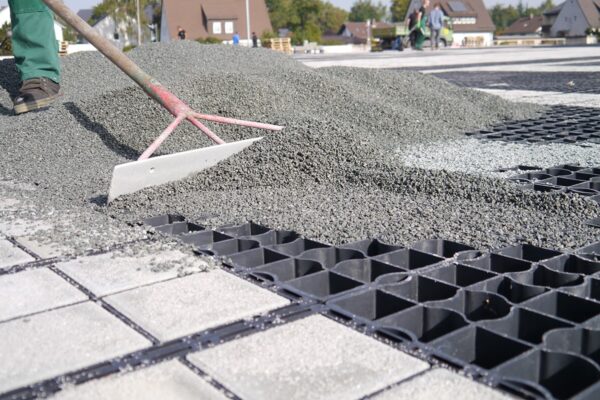 Kies wird mit großflächig mit einer Schaufel in die ECORASTER Bodengitter verteilt.