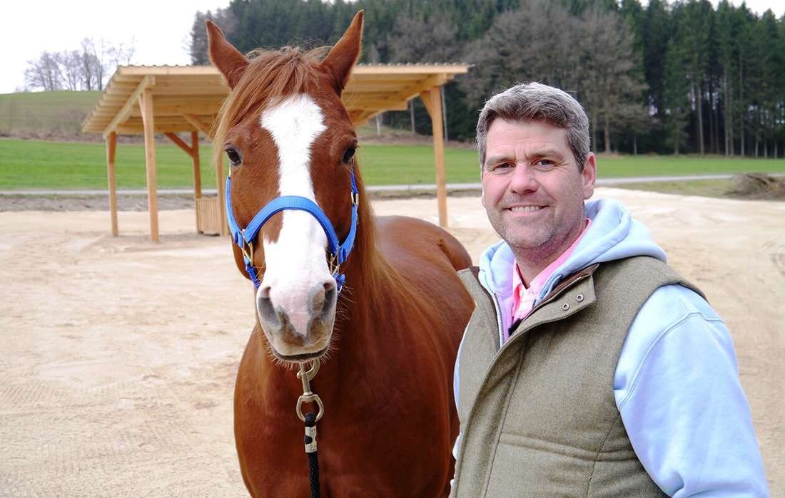 Pferd und Bernd Hackl befinden sich auf einem Reitplatz und schauen in die Kamera 