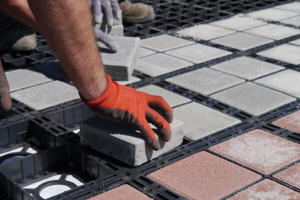 Hand mit Sicherheitshandschuhen setzt einen hellen Betonstein in dein ECORATER Bloxx Modul