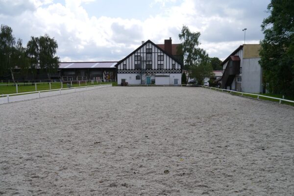 Großflächiger Reitplatz mit Fachwerkhaus im Hintergrund