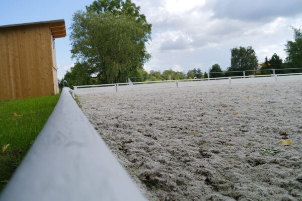 Nahansicht der Randeinfassung eines Reitplatzes mit Bäumen und Hütte im Hintergrund