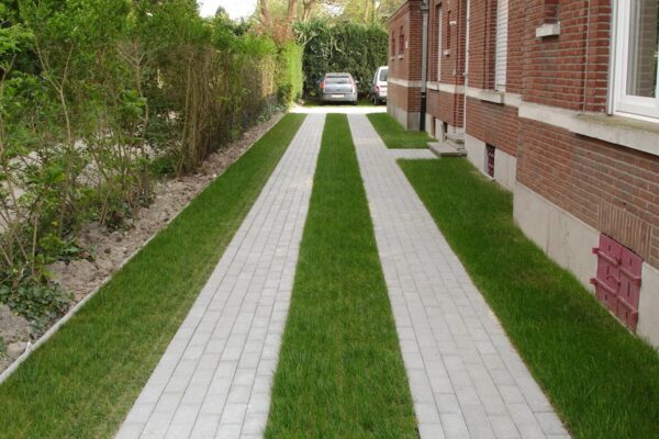 Zufahrt mit Betonfahrstreifen und begrünten ECORASTER Flächen entlang eines Backsteinhauses
