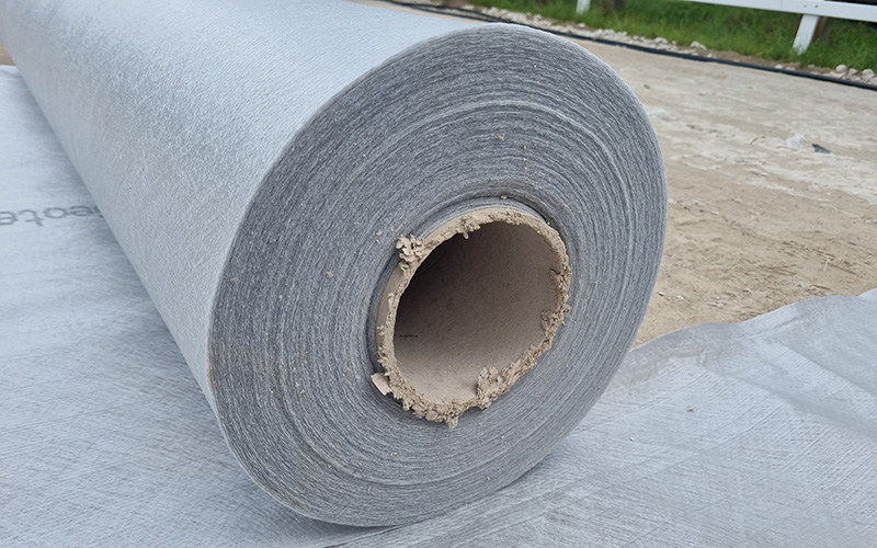 Eine große Rolle Bauvlies wird auf einem sandigen Boden ausgerollt