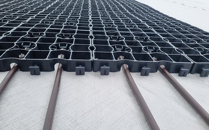 Eine Fläche Ecoraster E40 Aqua mit Wasserrohren liegen unbefüllt auf einem weißen Bauvlies